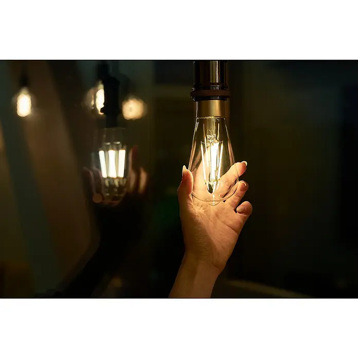 Shelly Smart-LED-Lampe Vintage ST64 - E27, Dimmbar, Warmweiß, 750 lm, 7 W - Nahaufnahme einer Hand, die eine dekorative Edison-Glühbirne hält, die ein warmes, stimmungsvolles Licht ausstrahlt. Schafft eine gemütliche Atmosphäre.