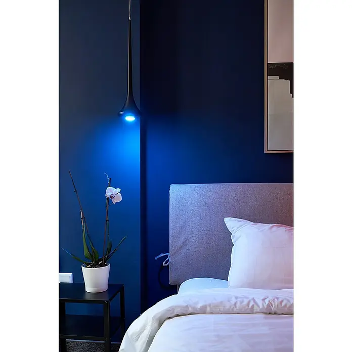 Shelly Smart-LED-Lampe Duo - RGBW GU10 - GU10, Dimmbar, Warmweiß, 400 lm, 5 W - Schlafzimmer mit Bett, Nachttisch, Pflanze und einer auffälligen Hängelampe mit blauem Licht.
