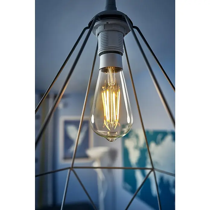 Shelly Smart-LED-Lampe Vintage ST64 - E27, Dimmbar, Warmweiß, 750 lm, 7 W - Nahaufnahme einer stilvollen Edison-Glühbirne in einem geometrischen Lampenschirm, die warmes Licht ausstrahlt und eine gemütliche Atmosphäre erzeugt.
