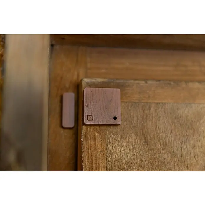 Shelly Fenster- & Türsensor BLU Door/Window - Bluetooth, Braun, Batteriebetrieben - Nahaufnahme eines Holz-Türsensors und seines Magneten auf einer Holztür, Fokus auf das Sicherheitssystem.