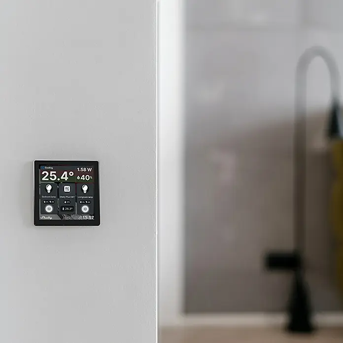Shelly Touchscreen-Bediengerät Wall Display - Schwarz, 30 x 85 x 85 mm - Intelligentes Home-Panel an einer weißen Wand mit Anzeige von Temperatur, Stromverbrauch und anderen intelligenten Haussteuerungen.