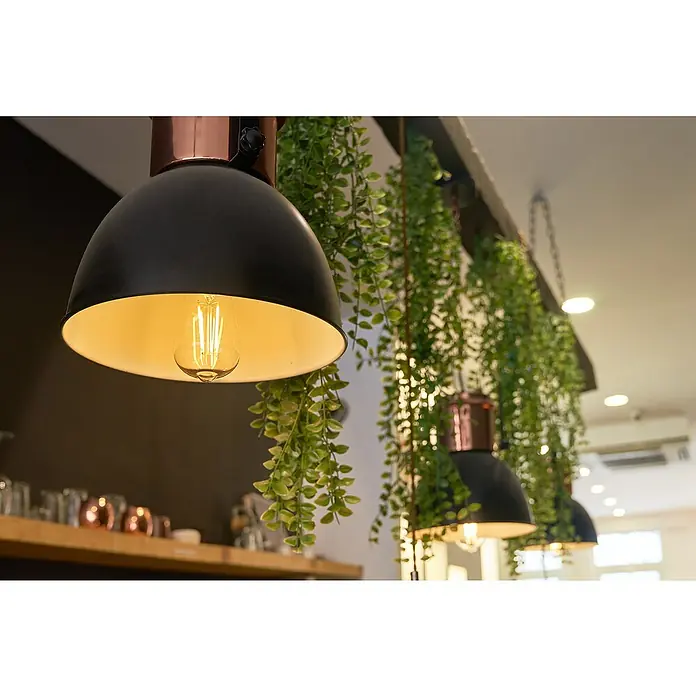 Shelly Smart-LED-Lampe Vintage ST64 - E27, Dimmbar, Warmweiß, 750 lm, 7 W - Nahaufnahme von stilvollen Pendelleuchten mit Glühbirnen und dekorativem Grün. Das moderne Design akzentuiert jeden Raum auf elegante Weise.