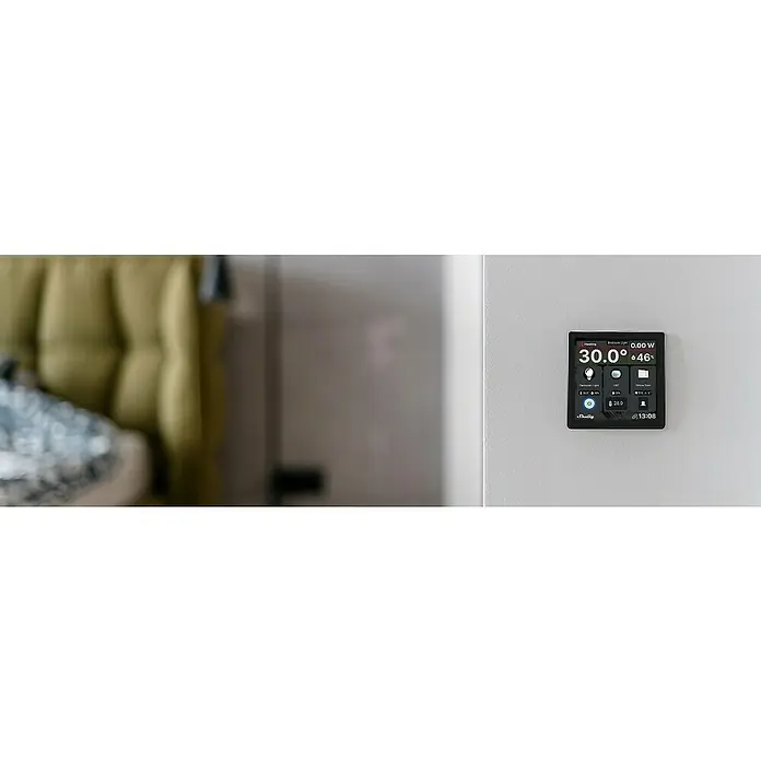 Shelly Touchscreen-Bediengerät Wall Display - Schwarz, 30 x 85 x 85 mm - Nahaufnahme eines Shelly-Smart-Home-Geräts an einer weißen Wand, das Temperatur und andere Haussteuerungsfunktionen anzeigt.