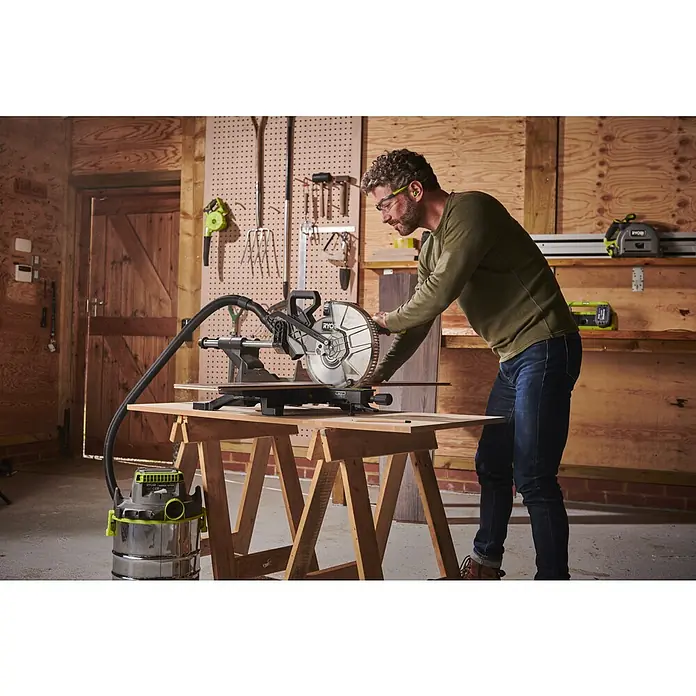 Ryobi ONE+HP Akku-Kapp- & Gehrungssäge RMS25418X-0 - 18 V, Ohne Akku, 4.100 U/min - Ein Mann bedient eine Ryobi-Kapp- und Gehrungssäge mit Staubsaugeranschluss in einer Werkstatt. Er trägt Schutzbrille und Ohrenschützer.
