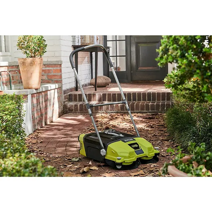 Ryobi ONE+ Akku-Handkehrmaschine R18SW3-0 - 18 V, Ohne Akku, Behältervolumen: 17 l - Der Ryobi Kehrmaschine mit Akku ist auf einem Ziegelweg vor einer Haustür platziert und bereit für die Reinigung.