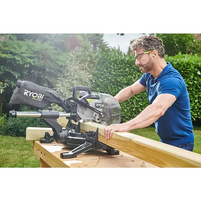 Ryobi ONE+HP Akku-Kapp- & Gehrungssäge RMS25418X-0 - 18 V, Ohne Akku, 4.100 U/min - Ein Mann benutzt eine Ryobi-Kappsäge, um ein Holzbrett im Freien zu schneiden, wobei er Schutzbrille und Ohrenschützer trägt.