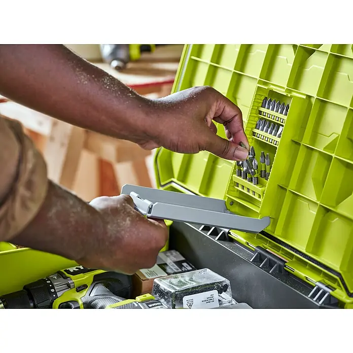 Ryobi Link Werkzeugkoffer RSL201 Trolley - L x B x H: 57 x 49,5 x 39 cm, Kunststoff, 2 Räder - Nahaufnahme einer Person, die einen Schraubenzieherbit aus einem Ryobi-Werkzeugkasten mit verschiedenen Bits und Zubehör entnimmt.