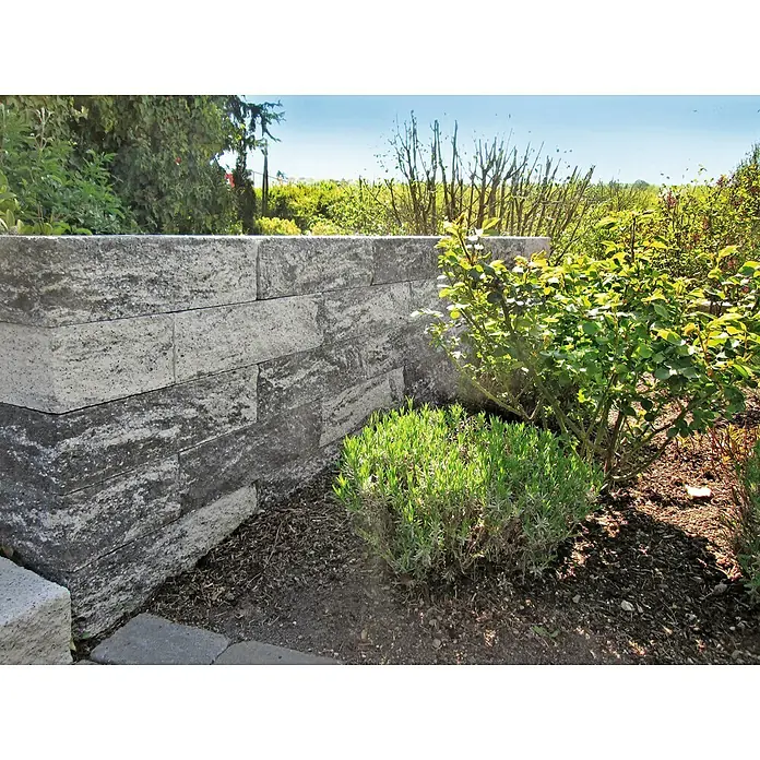Christoph Mauerstein Rustikalblock - 50 x 12,5 x 14 cm, Anthrazit/Weiß, Beton - Eine graue Steinmauer, eingebettet in üppiges Grün, bietet eine robuste und natürliche Gartengestaltung.