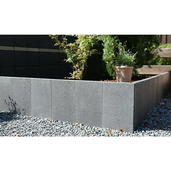 Christoph L-Stein - Anthrazit, 33 x 30 x 60 cm, Stärke: 4,3 cm - Nahaufnahme einer grauen Gartenmauer aus Betonsteinen, die eine erhöhte Beeteinfassung bildet, umgeben von Kies und Bepflanzung.