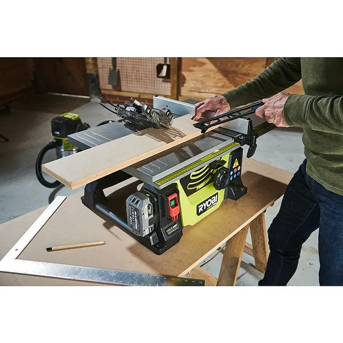 Ryobi ONE+HP Akku-Tischkreissäge RTBS18X-0 - 18 V, Ohne Akku, Durchmesser Sägeblatt: 210 mm - Ryobi ONE+ HP Tischsäge im Einsatz mit Holzbrett und Zubehör für präzise Schnitte in einer Werkstattumgebung.