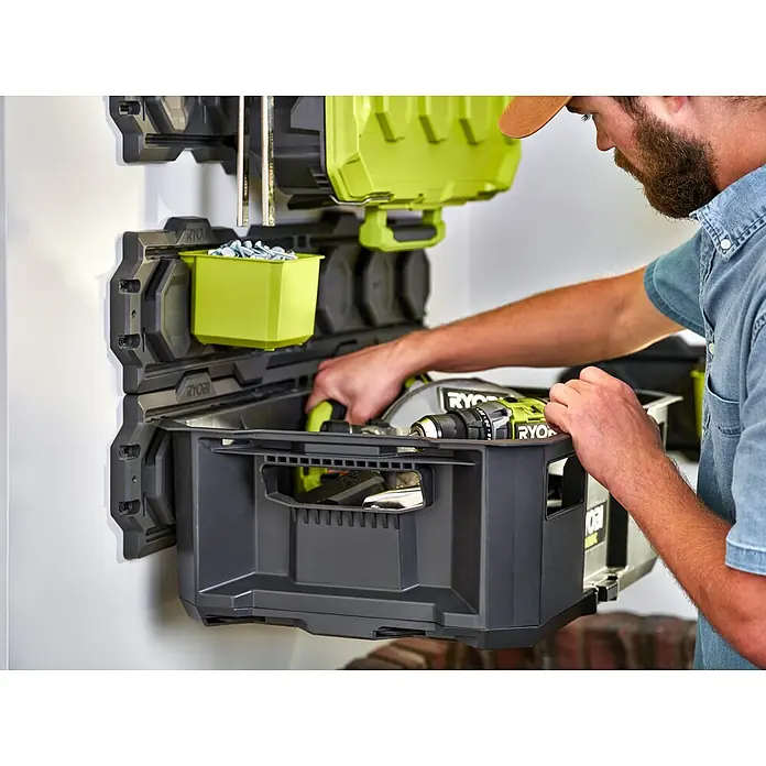Ryobi Link Werkzeugträger RSL104 - Kunststoff - Ein Mann ordnet Werkzeuge in Ryobi Werkzeugaufbewahrungsbehältern an einer Wand, die ein organisiertes System zur Lagerung bietet.