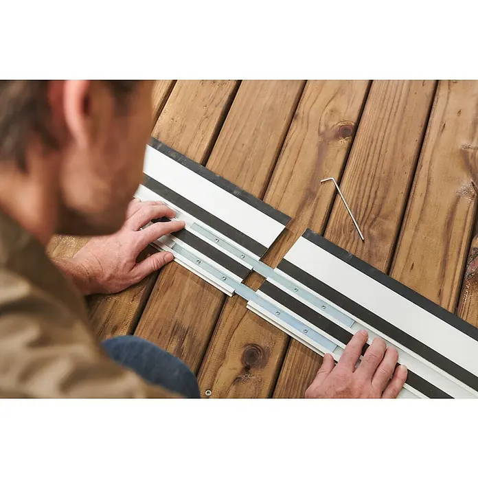 Ryobi ONE+HP Akku-Tauchsäge RPLS18X-0 - 18 V, Ohne Akku, Durchmesser Sägeblatt: 165 mm, Leerlaufdrehzahl: 4.300 U/min - Ein Mann befestigt eine Führungsschiene, um präzise Schnitte zu gewährleisten, mit einem Inbusschlüssel auf einer Holzoberfläche.