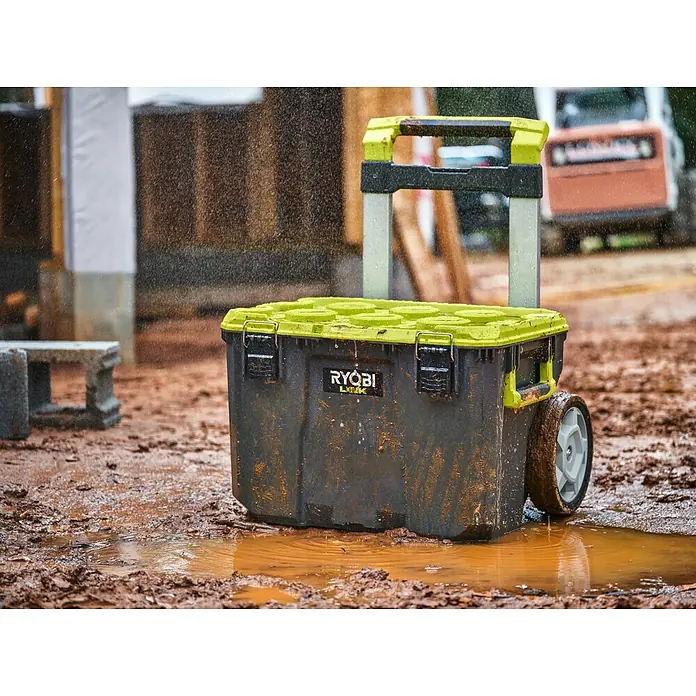 Ryobi Link Werkzeugkoffer RSL201 Trolley - L x B x H: 57 x 49,5 x 39 cm, Kunststoff, 2 Räder - Werkzeugkiste von Ryobi im Schlamm. Der Trolley ist schmutzig und steht auf einer Baustelle im Regen.