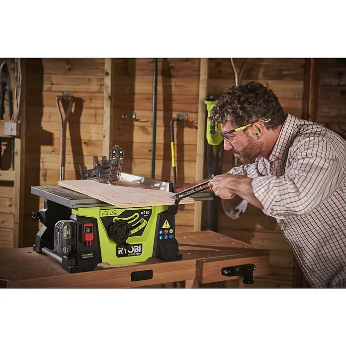 Ryobi ONE+HP Akku-Tischkreissäge RTBS18X-0 - 18 V, Ohne Akku, Durchmesser Sägeblatt: 210 mm - Ein Mann benutzt eine Ryobi Tischkreissäge, um Holz zu schneiden. Er trägt dabei Schutzbrille und Gehörschutz für die Sicherheit.