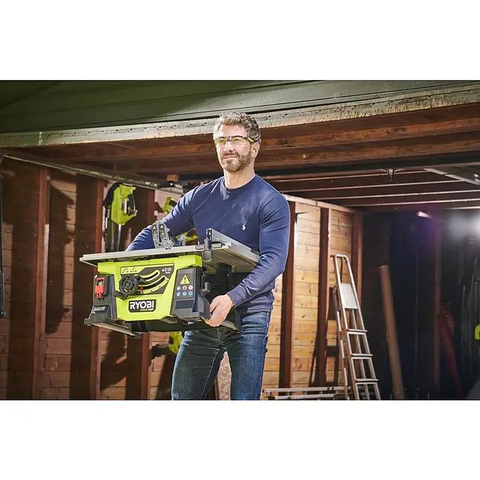 Ryobi ONE+HP Akku-Tischkreissäge RTBS18X-0 - 18 V, Ohne Akku, Durchmesser Sägeblatt: 210 mm - Ein Mann trägt eine Ryobi Tischkreissäge. Die Säge ist gelb und schwarz, während der Mann Schutzkleidung trägt.