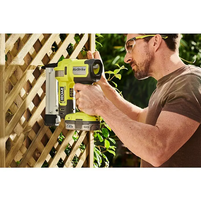 Ryobi ONE+ Akku-Tacker R18GS18-0 - 18 V, Li-Ionen, Ohne Akku - Ein Mann befestigt ein Holzgitter mit einem Ryobi Akku-Nagler. Das gelb-schwarze Werkzeug ist gut sichtbar und bereit für den Einsatz.