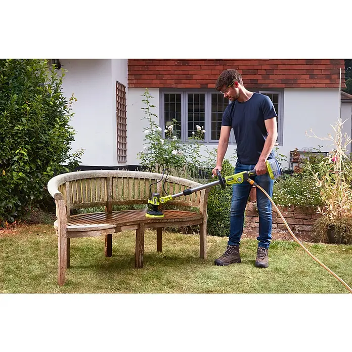 Ryobi ONE+ Akku-Reinigungsbürste RWTS18-0 - 18 V, Ohne Akku - Ein Mann reinigt eine Gartenbank mit einem Ryobi-Gerät. Das Gerät hat eine Bürste und einen Wasserschlauch für eine effektive Reinigung.