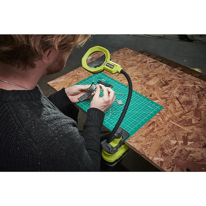 Ryobi ONE+ Akku-Lupenleuchte RML18-0 - 18 V, Ohne Akku - Nahaufnahme einer Person, die mit einer RYOBI-Arbeitsplatzleuchte an einer Uhr arbeitet, die auf einer Werkbank liegt.