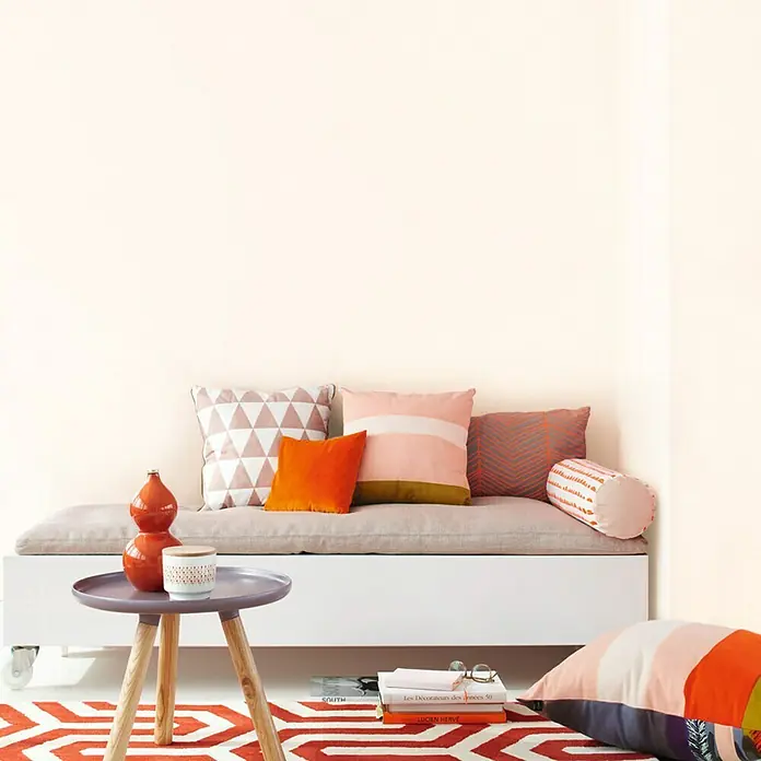 SCHÖNER WOHNEN-Farbe MyColour Wandfarbe - Magnolia, Matt, 10 l - Das Bild zeigt ein gemütliches Wohnzimmerarrangement mit einem niedrigen Sofa, bunten Kissen und einem kleinen, runden Tisch mit Deko-Objekten.