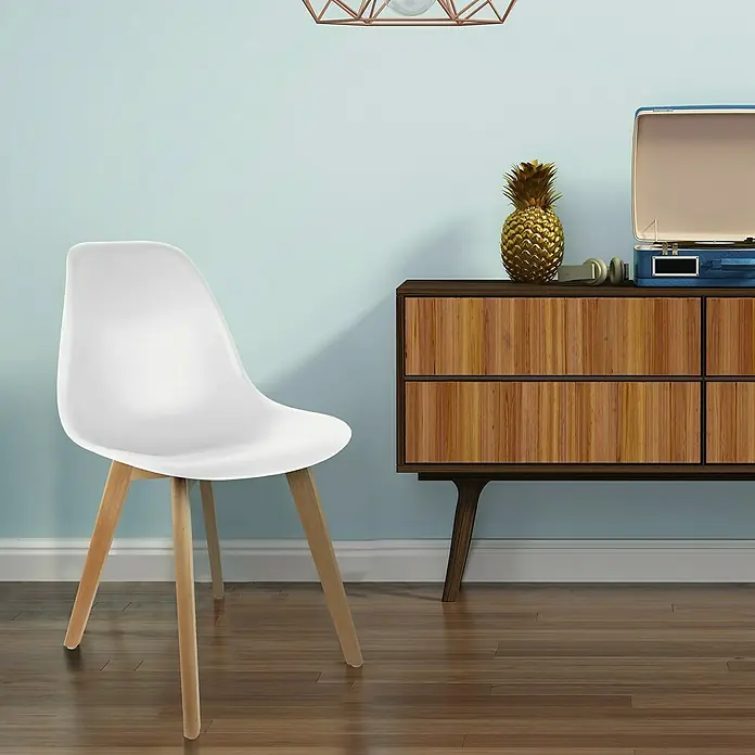 Home Deco Factory Silla Stockholm - Blanco, 4 pzs. - Una silla blanca con patas de madera frente a una pared azul claro, junto a un mueble de madera con una piña dorada y tocadiscos.