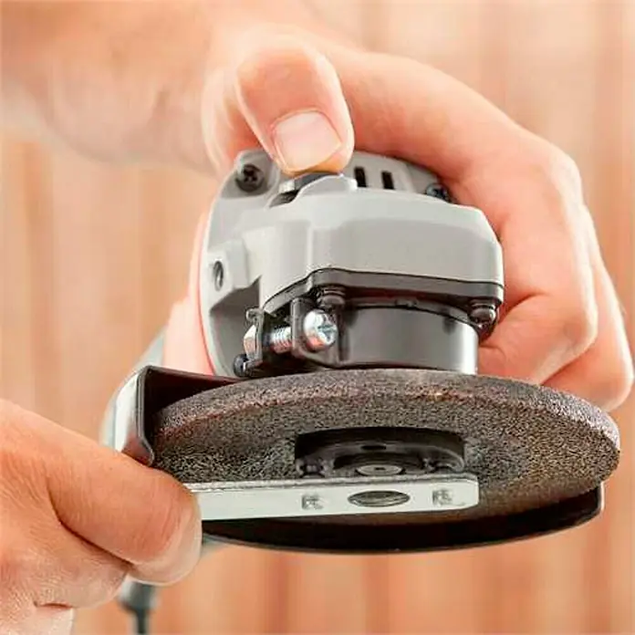Black+Decker Amoladora angular eléctrica BEG010 - 710 W, Diámetro disco: 115 mm, 12.000 r.p.m. - Primer plano de una persona que opera una máquina de rectificado. La máquina gris tiene una muela oscura y se acciona a mano.