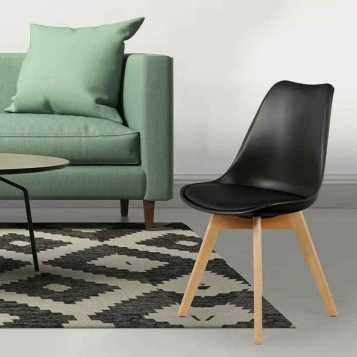 Silla Copenhague - Negro, 4 pzs. - Una elegante silla negra con patas de madera clara se encuentra sobre una alfombra estampada frente a un sofá color menta.