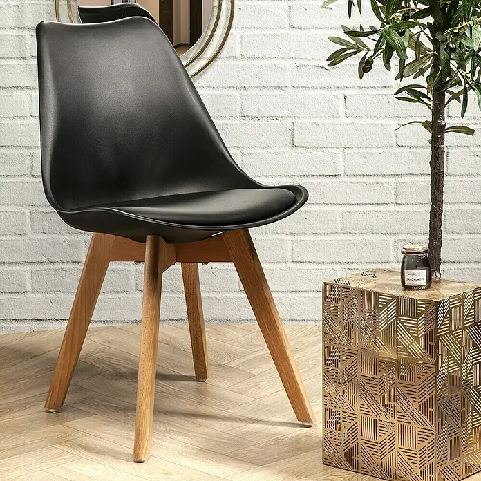 Silla Copenhague - Negro, 4 pzs. - Elegante silla negra con patas de madera junto a una mesa auxiliar dorada y planta de interior.
