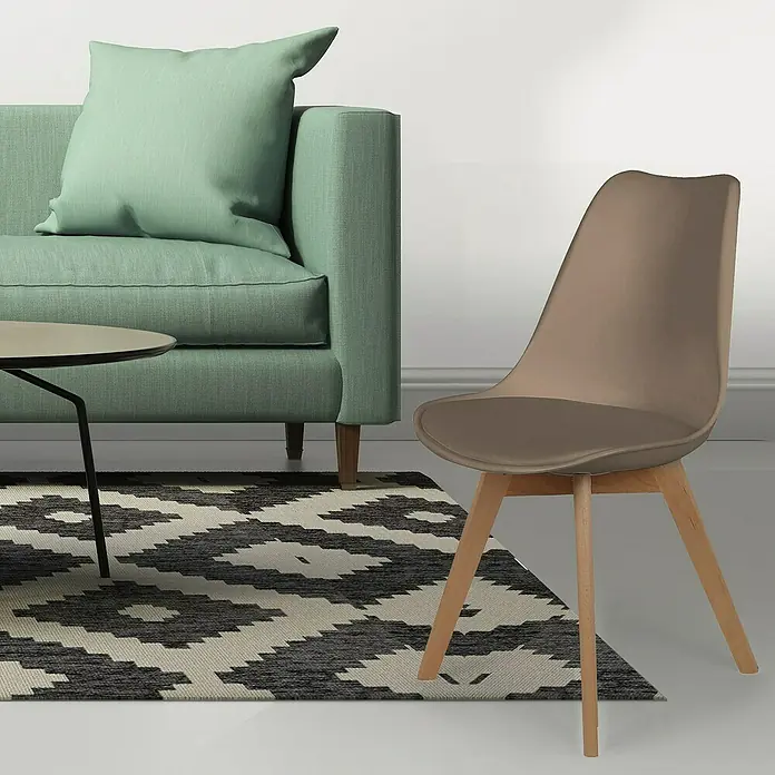 Home Deco Factory Silla Copenhague - Marrón, 4 pzs. - Una silla moderna con patas de madera sobre una alfombra estampada, junto a un sofá verde y una mesa pequeña. La silla tiene un asiento marrón.