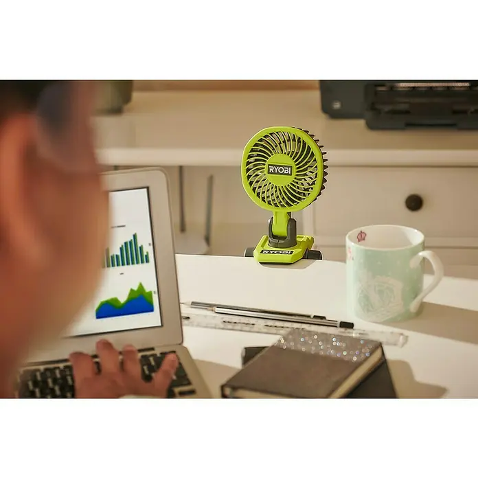 Ryobi 4V USB Akku-Ventilator RCF4-0 - 4 V, Ohne Akku - Ein grüner Ryobi-Clip-Ventilator steht auf einem weißen Schreibtisch, neben einem Laptop und einer Tasse, der für eine kühle Brise sorgt.