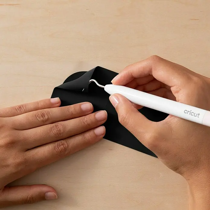 Cricut Joy Xtra Vinylfolie Smart Permanent - 3 -tlg., Classics, 24,1 x 30,5 cm - Nahaufnahme einer Hand, die mit einem Cricut Werkzeug schwarzes Vinyl entgittert, um unerwünschte Teile zu entfernen, ideal für DIY-Projekte.