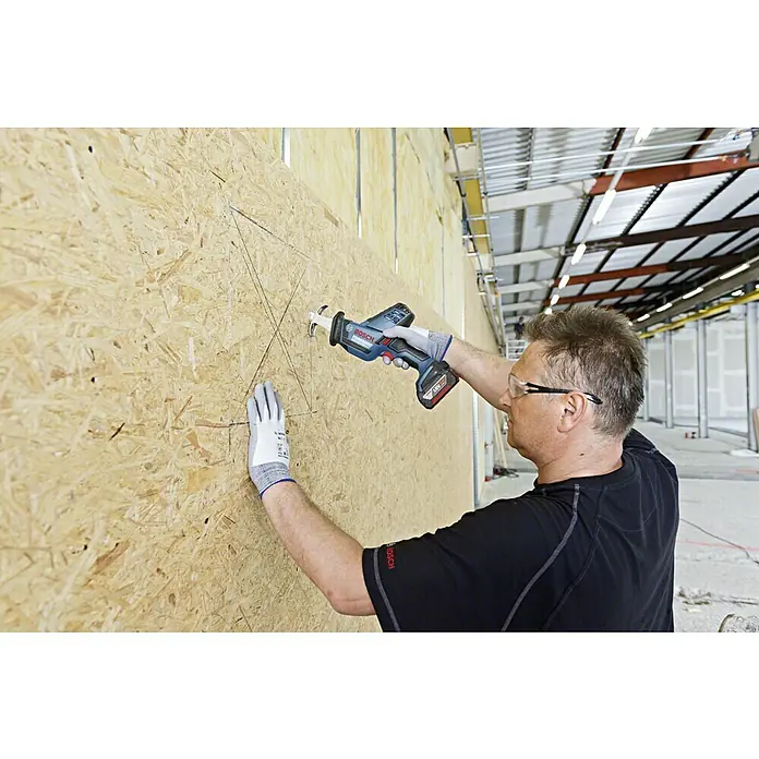 Bosch Professional AMPShare 18V Akku-Säbelsäge GSA 18 V-LI C L-Boxx - 18 V, Ohne Akku, 3.050 /min, Koffer - Ein Mann benutzt eine Bosch Säbelsäge, um ein Loch in eine Holzwand zu sägen. Er trägt dabei Schutzbrille und Handschuhe.
