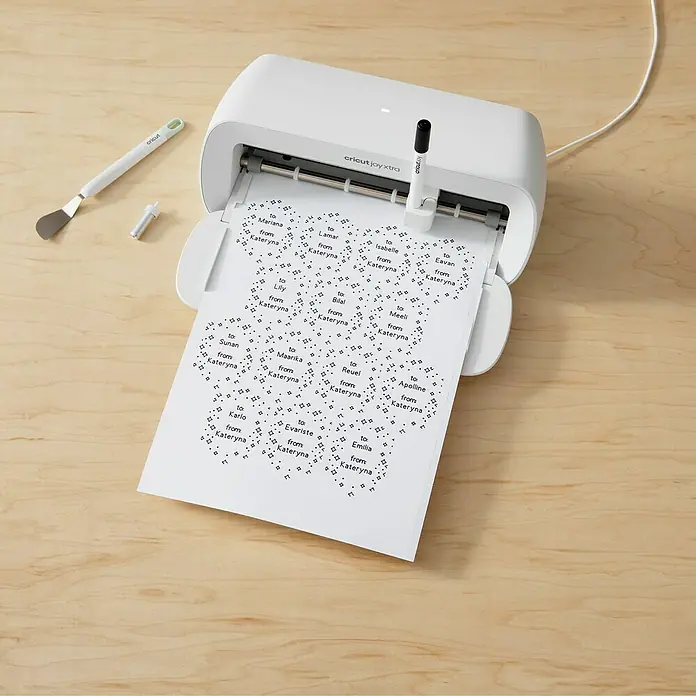 Cricut Joy Xtra Vinylfolie Smart Label Beschreibbar Permanent - 3 Stk., Weiß - Cricut Joy Xtra Schneideplotter beim Drucken personalisierter Aufkleber mit Namen auf einem hellen Holztisch.