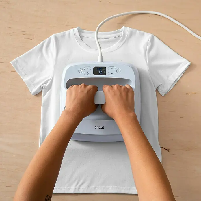 Cricut Aufbügelfolie Light Fabrics - 5 Stk., Weiß, L x B: 29,7 x 21 cm - Nahaufnahme einer Person, die ein weißes T-Shirt mit einer Cricut EasyPress Bügelmaschine bearbeitet. Die Maschine ist auf 330 Grad Fahrenheit eingestellt.