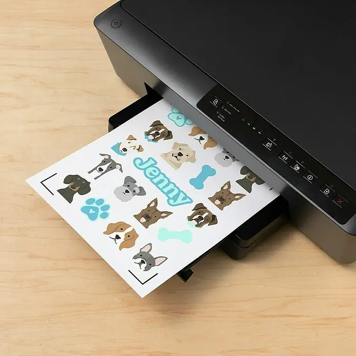 Cricut Aufkleber Set Holografisch Bedruckbar und Wasserfest - 5 Stk., Transparent Holografisch, 21 x 29,7 cm - Ein Tintenstrahldrucker druckt ein Blatt Papier mit Hundeaufklebern und dem Namen "Jenny" darauf, ideal zum Personalisieren von Gegenständen.