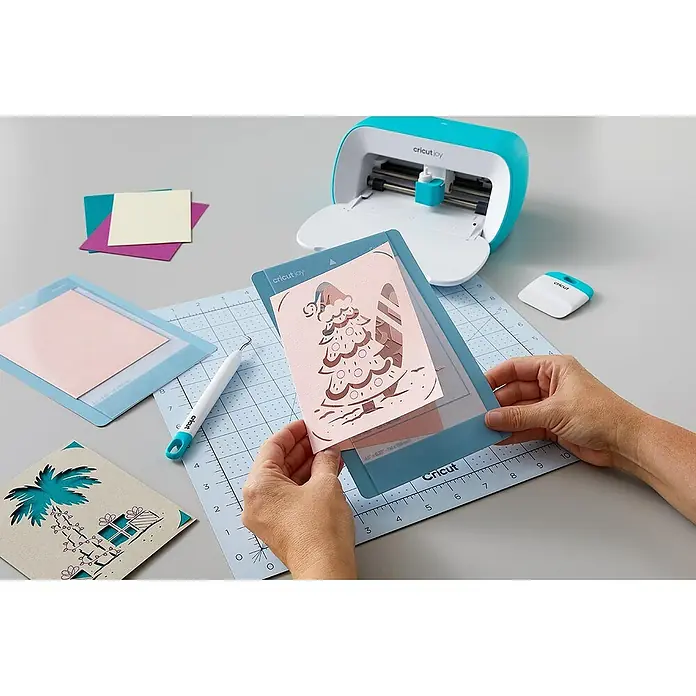 Cricut Joy Schneideplotter Starter Bundle - Bluetooth, Schnittbreite: 10,4 cm, Schnittlänge: 1,2 m - Nahaufnahme einer Cricut Joy Schneidemaschine in Türkis, die auf einem Tisch steht, umgeben von Bastelmaterialien und Werkzeugen für kreative Projekte.