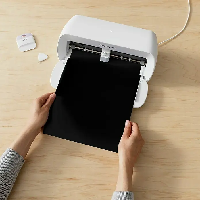 Cricut Joy Xtra Vinylfolie Smart Permanent - 3 -tlg., Elegance, 24,1 x 30,5 cm - Nahaufnahme eines Cricut Joy Xtra Schneideplotters mit eingelegtem schwarzem Vinylblatt, bereit zum Schneiden für Bastelprojekte.