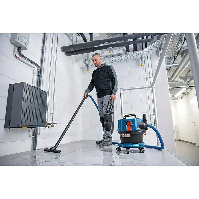 Bosch Professional AMPShare 18V Akku-Nass-Trockensauger GAS 18V-12 MC - Ohne Akku, 18 V, Behältervolumen: 12 l - Ein Mann reinigt einen Raum mit einem Bosch Professional Nass-Trockensauger. Der Sauger ist blau-schwarz und steht auf Rollen.