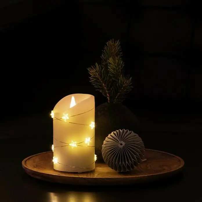 Konstsmide LED-Kerze - Cremeweiß, Ø x H: 7,5 x 13,5 cm, Echtwachs - Dekorative LED-Kerze mit Sternenlichtern auf einem Holztablett, ergänzt durch Tannenzweige und eine Papierdekoration.
