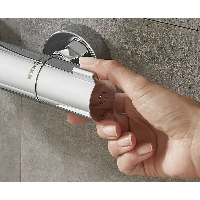 Hansgrohe Grifo con termostato MyFox - Ancho: 29,6 cm, Cromo, Resplandeciente - Una mano opera un termostato de ducha cromado con indicador de temperatura en una pared gris, para un control preciso.