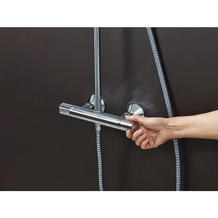 Hansgrohe Vernis Blend Sistema de ducha 200 - Caudal de agua: 6,8 l/min, Cromo - Una mano ajusta el grifo de la ducha cromado para ajustar la temperatura, que está montado en una pared oscura. La manguera también es visible.