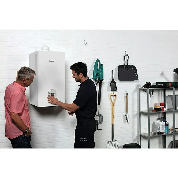 Bosch Caldera de gas Condens GC 1200 W 20/24 - 24 kW, 6 l, Gas natural, Display multifunción - Una caldera Bosch blanca cuelga de una pared de ladrillo blanco mientras dos hombres la miran y ajustan los parámetros.