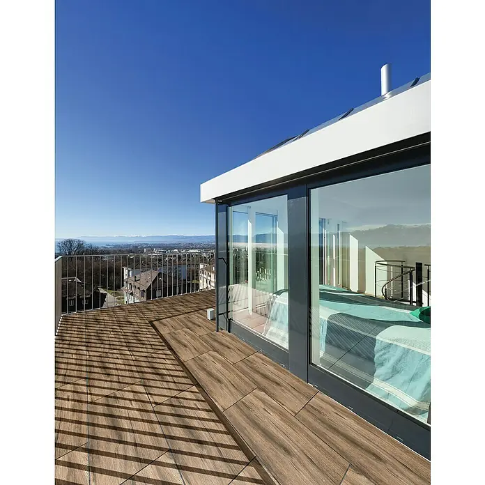Terrassenfliese Strobus - 40 x 120 x 2 cm, Ebony/Braun, Matt - Die Terrasse ist mit modernen, braunen Holzfliesen ausgelegt, die einen warmen und einladenden Außenbereich schaffen. Die Verlegung erfolgt im Fischgrätmuster.