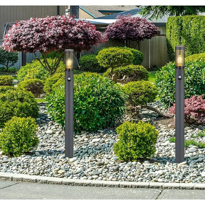Globo Boston Außenwegeleuchte - 15 W, Farbe Gehäuse: Anthrazit, Ohne Leuchtmittel - Eine Nahaufnahme von zwei modernen grauen Gartenleuchten, die einen beleuchteten Gartenweg mit Zierkies und üppigem Grün erhellen.