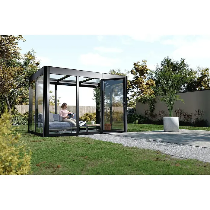 SunElements Gewächshaus SunGarden Infinity 2.1 - Außenmaß inkl. Dachüberstand (B x T): 233 x 128 cm, Material Seitenwand: Kunststoff, 6 mm, Anthrazit-Metallic - Bild eines modernen Glasgartenhauses mit schwarzem Rahmen, einer Frau, die drinnen liest, und einer gepflasterten Terrasse, die zu einem üppigen Garten führt.