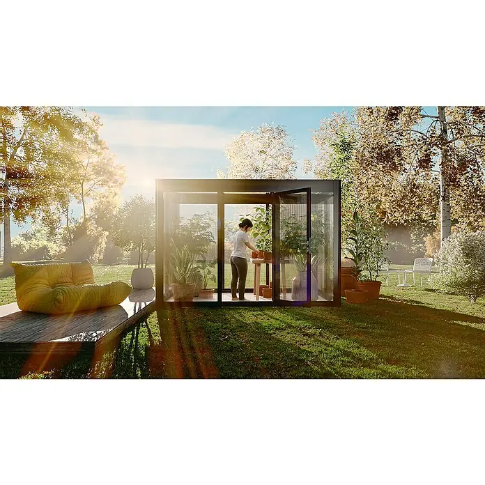 SunElements Gewächshaus SunGarden Select 5.2 - Außenmaß inkl. Dachüberstand (B x T): 548 x 233 cm, Material Seitenwand: Kunststoff, 10 mm, Anthrazit-Metallic - Eine Frau im Gewächshaus mit Pflanzen, umgeben von einem Garten mit einem Sessel.