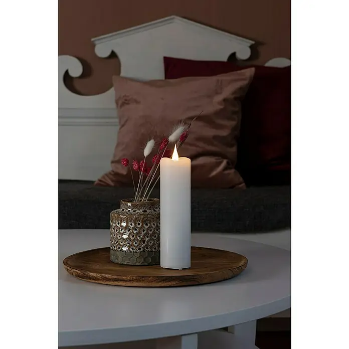 Konstsmide LED-Kerze - Weiß, Ø x H: 7,8 x 22 cm, Echtwachs - Nahaufnahme einer weißen LED-Kerze und einer Vase mit Blumen auf einem Holztisch, die eine gemütliche und warme Atmosphäre schaffen.