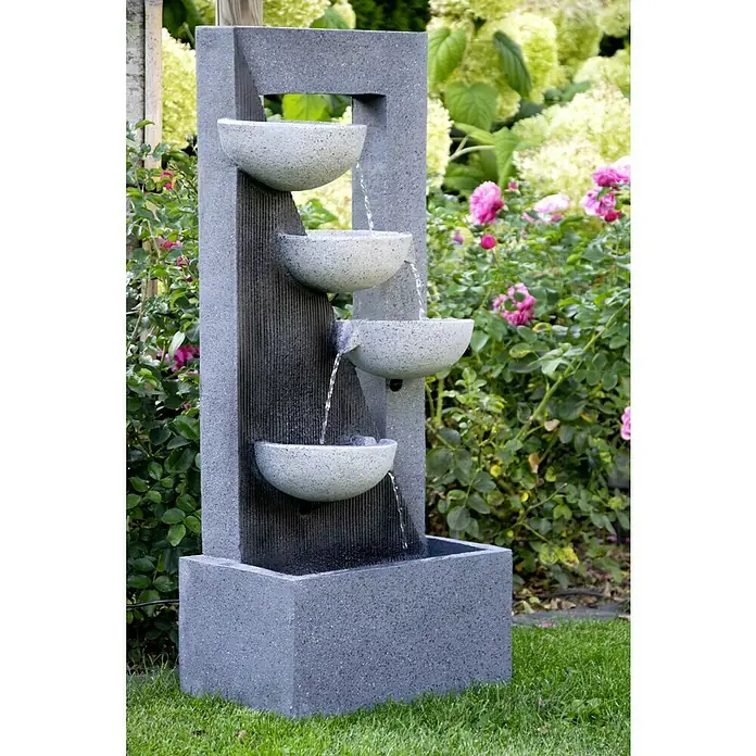 Dobar Kunststeinbrunnen - 40 x 25 x 92 cm - Bild einer modernen mehrstufigen Gartenbrunnenanlage mit Wasser, das in verschiedenen Becken kaskadenartig herabfließt, umgeben von üppigem Grün und Blumen.