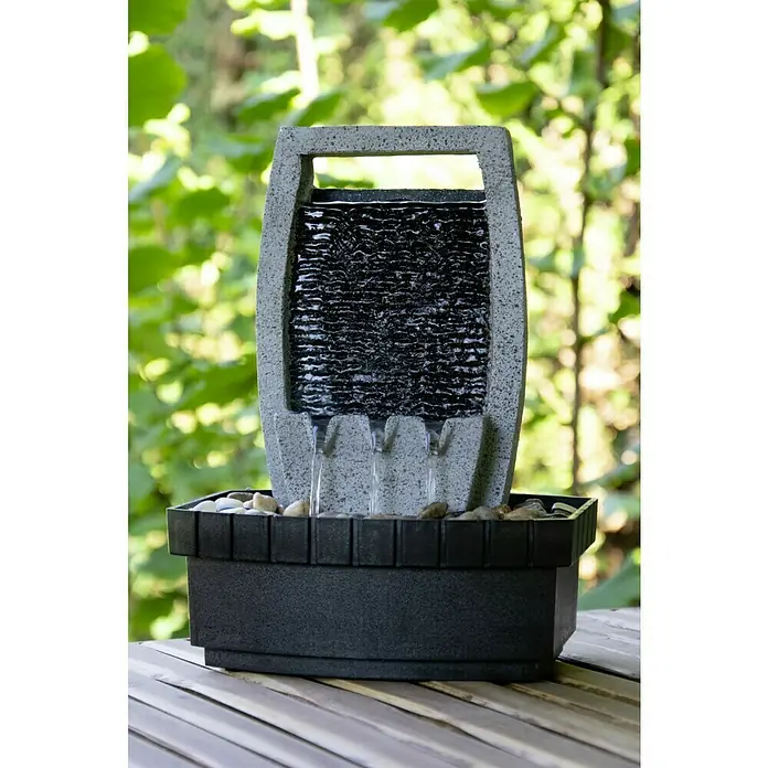 Dobar Gartenbrunnen - 20,5 x 16,5 x 28 cm, Kunststoff, Grau/Schwarz - Nahaufnahme eines Zimmerbrunnens mit grauem Rahmen und schwarzem Wasserfall, der auf einem Holztisch vor grünem Hintergrund steht.