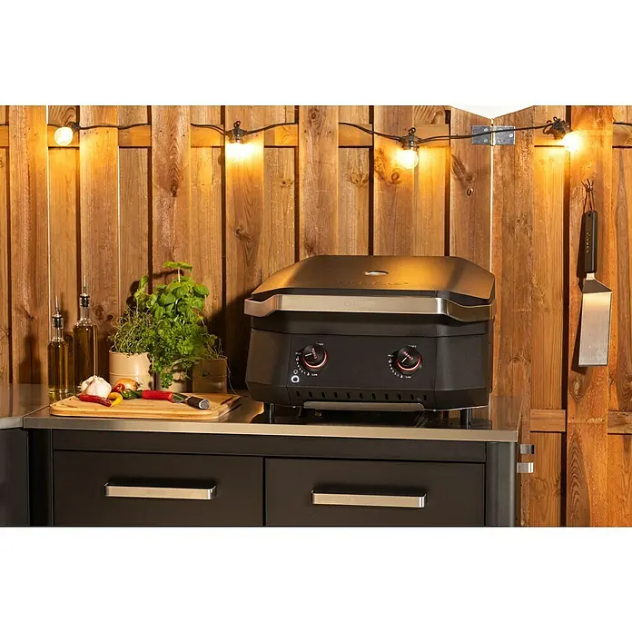 Cozze Gasgrill G 500Grillfläche (B x T): 53,5 x 41,8 cm, 5 kW, Anzahl Brenner: 2 Stk. - Nahaufnahme eines schwarzen Grills mit silbernen Akzenten auf einer Arbeitsfläche im Freien, umgeben von Kräutern und Gewürzen.