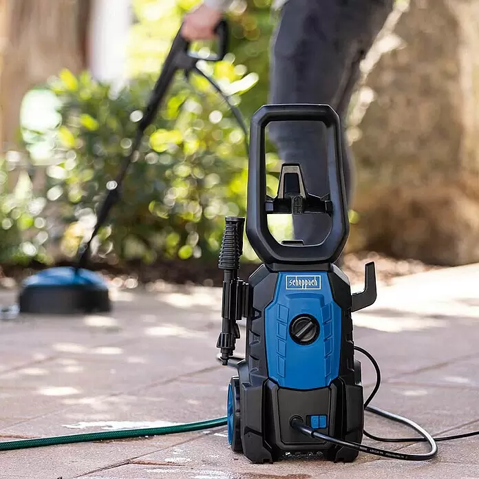 Scheppach Hochdruckreiniger HPC1600-Kit - 135 bar, 1.600 W, Fördermenge: 420 l/h - Blaue und schwarze Scheppach Hochdruckreiniger in Gebrauch auf einer gepflasterten Terrasse, mit einer Person, die einen Flächenreiniger bedient.